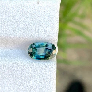 May include: Oval-shaped green gemstone with a blue hue, set on a white background.