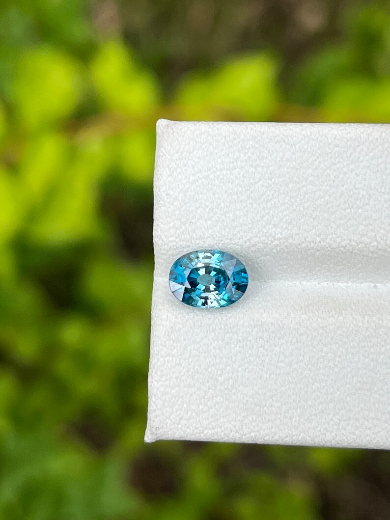 May include: A teal blue oval-shaped gemstone on a white background.