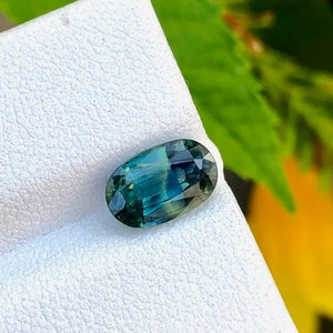 May include: A green and blue oval-shaped gemstone on a white background.