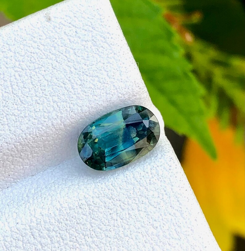 May include: A green and blue oval-shaped gemstone on a white background.