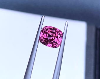 Op de afbeelding: Een levendige roze edelsteen met een kussen-slijpsel, vastgehouden door een pincet tegen een witte achtergrond.
