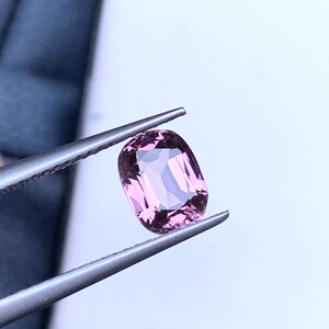 May include: A pink oval-shaped gemstone held by tweezers against a white background.