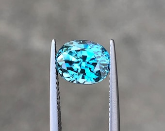 May include: A light blue oval-shaped gemstone held by tweezers. The gemstone has a faceted cut and a bright, clear colour.