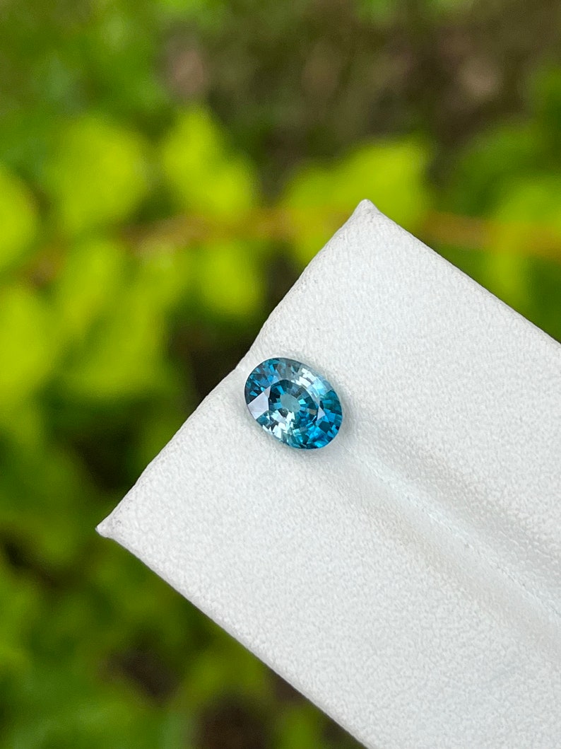 May include: A teal blue oval gemstone with a slight green hue, set on a white background.