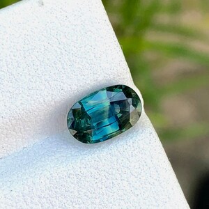 May include: A green oval gemstone with a blue hue, set on a white background.