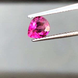 Puede incluir: Una piedra preciosa rosa en forma de pera sostenida por unas pinzas.