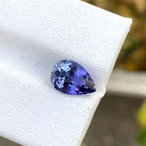 K&ouml;nnte beinhalten: Ein birnenf&ouml;rmiger Edelstein mit einer tiefblauen bis violetten Farbe. Der Edelstein ist auf einem wei&szlig;en Hintergrund platziert.