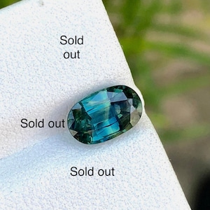 May include: A green oval gemstone with a faceted cut. The gemstone is on a white surface with the text "Sold out" written on it.