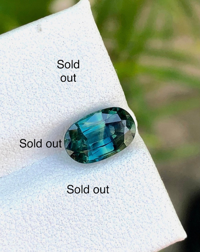 May include: A green oval gemstone with a faceted cut. The gemstone is on a white surface with the text "Sold out" written on it.