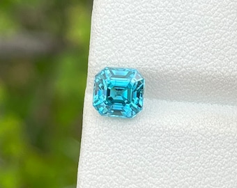 May include: A light blue gemstone with a square emerald cut. The gemstone is on a white background.