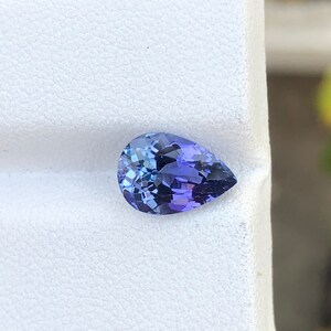 K&ouml;nnte beinhalten: Ein birnenf&ouml;rmiger, violetter Edelstein mit einem hellblauen Farbton. Der Edelstein ist auf einem wei&szlig;en Hintergrund platziert.
