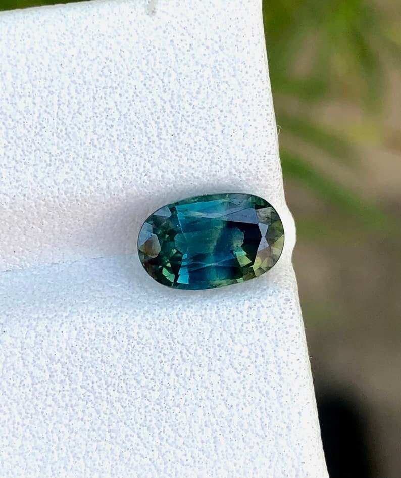 May include: Oval-shaped green gemstone with a blue hue, set on a white background.