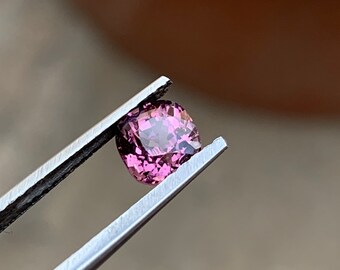 Op de afbeelding: Een roze edelsteen met een kussen-slijpsel, vastgehouden door een pincet.