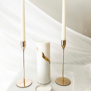 May include: Two gold candle holders with white candles, a white pillar candle with gold accents, and a heart-shaped white candle holder.