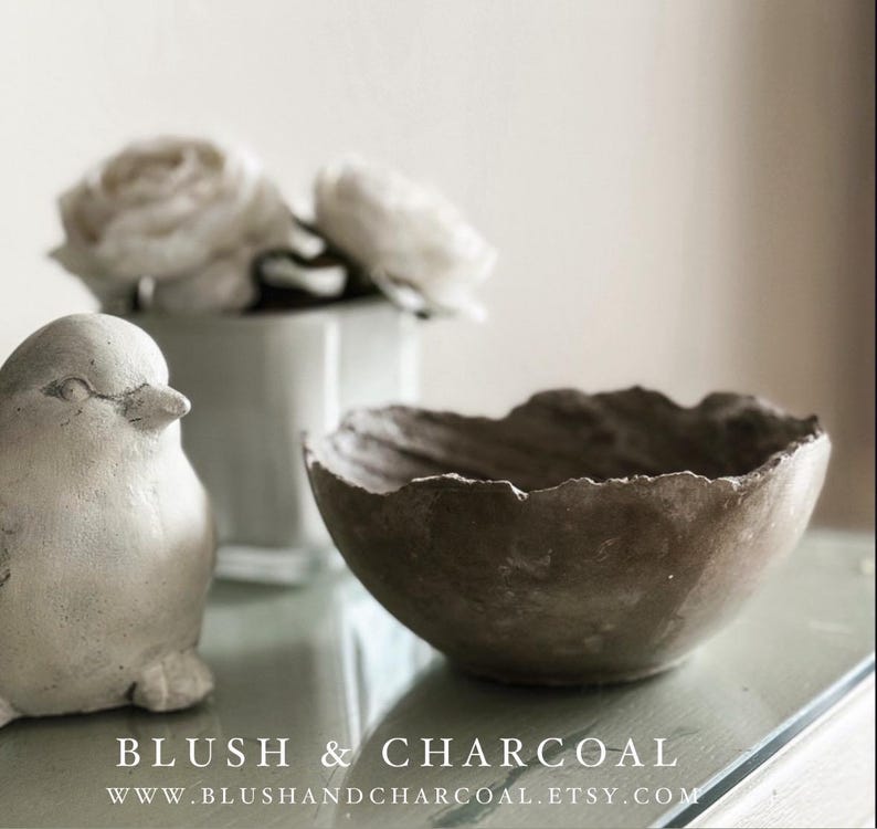 May include: A small, dark brown bowl with a rough, uneven, and textured rim. Beside the bowl sits a light-colored, smooth, rounded bird figurine. The text "BLUSH & CHARCOAL" and "WWW.BLUSHANDCHARCOAL.ETSY.COM" is printed at the bottom of the image.