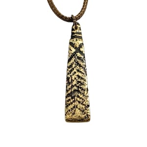 May include: A bronze-toned metal pendant with a tapered, rectangular shape and a textured, dark-etched herringbone pattern. The pendant hangs from a thin, brown braided cord, featuring a small metal loop at the top for attachment to the necklace.