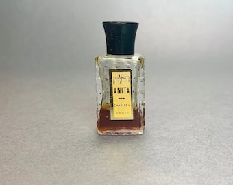 May include: A small, clear glass bottle of perfume with a black cap. The label is gold and says "parfum Anita Charles V Paris".