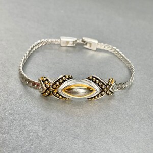 May include: A silver bangle bracelet with a gold-toned oval centerpiece. The centerpiece is decorated with small gold beads.