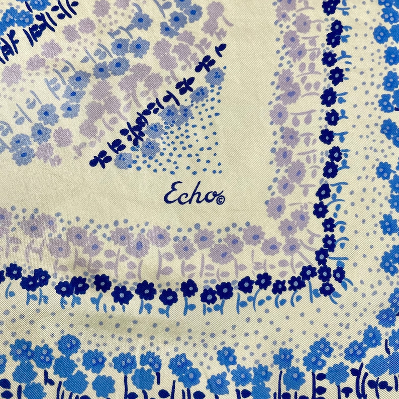 May include: A white silk scarf with a blue and purple floral pattern. The scarf has the word "Echo" printed in the center.