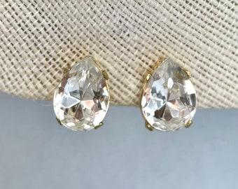 May include: A pair of gold teardrop-shaped earrings with clear crystal stones.