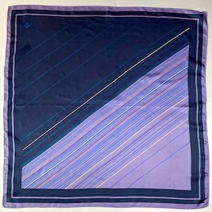 May include: A purple and navy blue silk scarf with a geometric pattern of diagonal lines. The scarf has a narrow border around the edges.