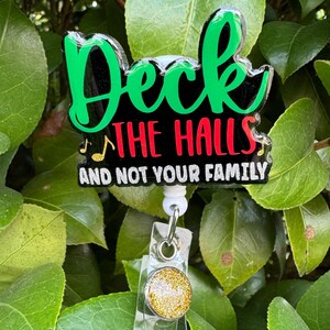 May include: A green, red, and black Christmas-themed badge holder with the text "Deck the Halls and not your family". The badge holder has a gold glitter charm.