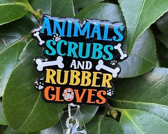 May include: A black badge reel with the words "ANIMALS, SCRUBS, AND RUBBER GLOVES" in blue, teal, yellow, and orange. The reel has a bone and paw print design, and a round, glittery blue charm.