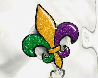 May include: A green, gold, and purple glitter fleur-de-lis charm attached to a clear plastic badge holder with a round, green, gold, and purple glitter button.