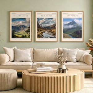 May include: Three framed landscape prints depicting mountain scenery. The prints are labelled "Scafell Pike," "Ben Nevis," and "Snowdon." Each print has a light-coloured frame and text at the top and bottom. They are displayed above a beige sofa.