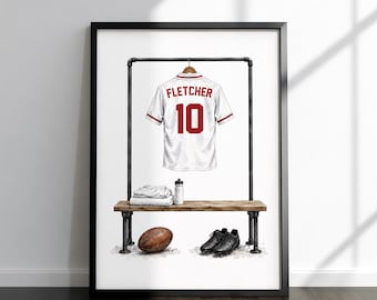 May include: A framed print featuring a white sports jersey with the name FLETCHER and the number 10 in red, hanging on a metal rack above a wooden bench. Below, a brown football, black cleats, a water bottle, and folded white towels.