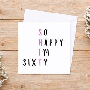 May include: A square white greeting card with black text that reads SO HAPPY I'M SIXTY. The letters S, H, I, and T are vertically aligned in pink to spell out a word. The card is accompanied by a matching white envelope.