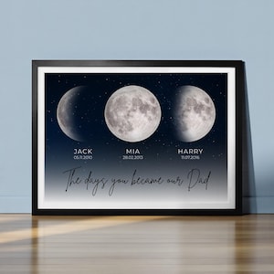 Pode incluir: Impressão emoldurada com três fases da lua contra um céu estrelado. Os nomes "JACK", "MIA" e "HARRY" e datas estão abaixo de cada fase da lua. O texto "The days you became our Dad" está escrito em itálico.