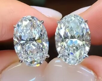 May include: A pair of oval-shaped diamond earrings set in a silver metal setting. The diamonds are clear and sparkly.
