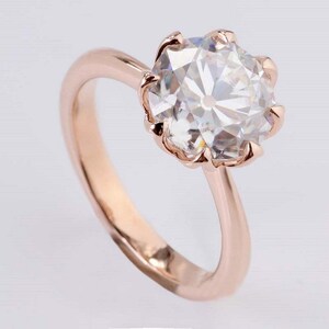 May include: A rose gold engagement ring with a large, clear, round-cut diamond set in a six-prong setting.