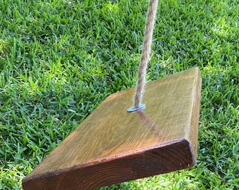 Puede incluir: Un asiento de columpio de madera con un acabado marrón natural y una cuerda colgando de un anillo de metal.