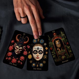 May include: Three tarot cards with detailed illustrations are displayed. The cards feature images of The Devil, The Moon, and Strength. The Devil card shows a horned figure surrounded by roses. The Moon card has a face with floral accents. The Strength card depicts a lion.
