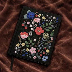 May include: Black journal with embroidered floral design. The cover is adorned with colourful embroidered flowers in red, pink, blue, yellow, and white, with green leaves and a butterfly. A black ribbon bookmark is visible.