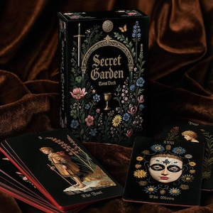 May include: A black tarot deck box and cards with floral and botanical illustrations. The box reads "Secret Garden Tarot Deck" in gold lettering. The cards feature detailed artwork and titles such as "The Fool" and "The Moon".