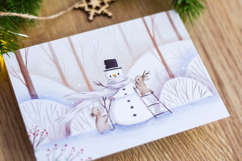 May include: A winter scene with a snowman wearing a white scarf and a black top hat. Two brown rabbits are standing near the snowman, one is on a ladder. The background is a snowy forest with white and brown trees.
