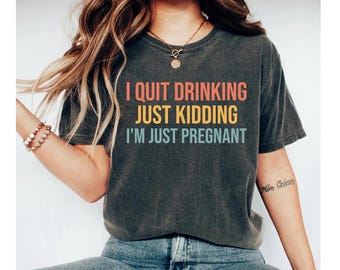 May include: A dark grey t-shirt with the text "I quit drinking just kidding I'm just pregnant" in rainbow colors.