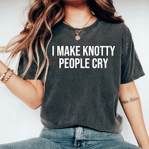 May include: A dark gray t-shirt with the text "I MAKE KNOTTY PEOPLE CRY" printed in white.