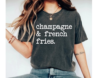 Może przedstawiać: Szary t-shirt z nadrukiem "champagne & french fries." w kolorze białym.