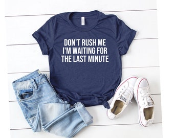 May include: A navy blue t-shirt with white text that reads "Don't rush me I'm waiting for the last minute". The shirt is paired with blue jeans and white sneakers.