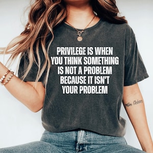 May include: A dark gray t-shirt with a white graphic print that reads "Privilege is when you think something is not a problem because it isn't your problem."