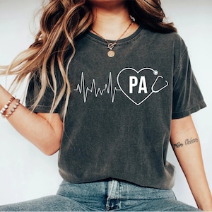 May include: A dark gray t-shirt with a white graphic of a heartbeat with a heart that says "PA" and a stethoscope.