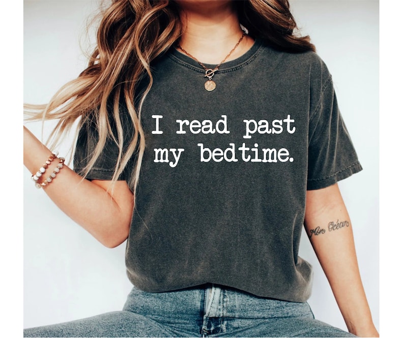 May include: A dark gray t-shirt with the text "I read past my bedtime." printed in white. The shirt is made of a soft, comfortable material and has a relaxed fit.