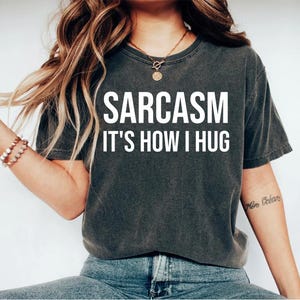 May include: A dark gray t-shirt with the text "SARCASM IT'S HOW I HUG" in white lettering.