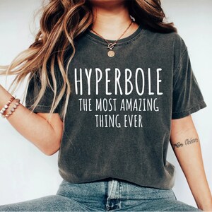 May include: A dark gray t-shirt with the text "HYPERBOLE THE MOST AMAZING THING EVER" printed in white.