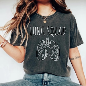 May include: Dark gray t-shirt with the words "LUNG SQUAD" in white, above a white illustration of lungs. The shirt has short sleeves and a crew neck.