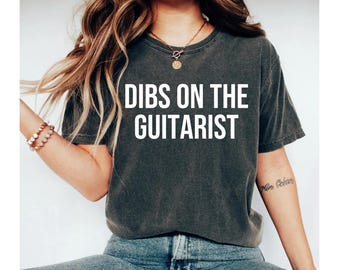 May include: A dark gray t-shirt with the text "DIBS ON THE GUITARIST" printed in white.
